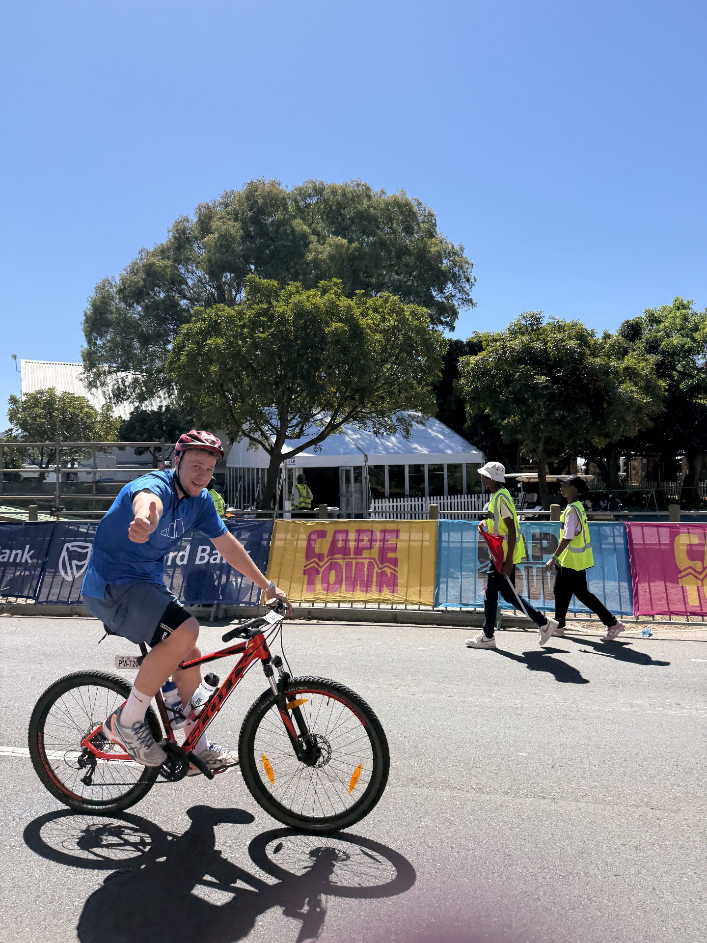 Matteo Buxman riding a mountain bike past Cape Town Cycle Tour banners, giving a thumbs up