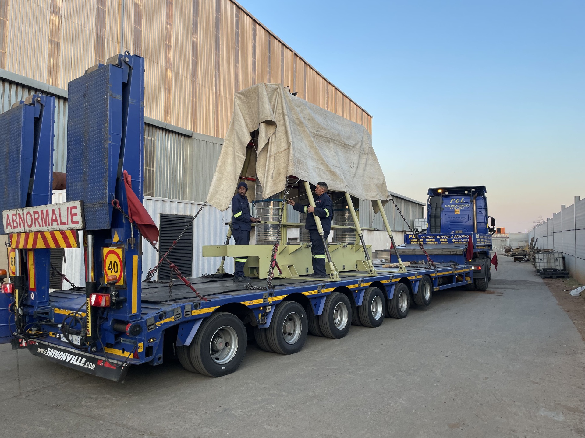 A transformer core assembly strapped to a blue Faymonville low-bed abnormal-load trailer at dawn